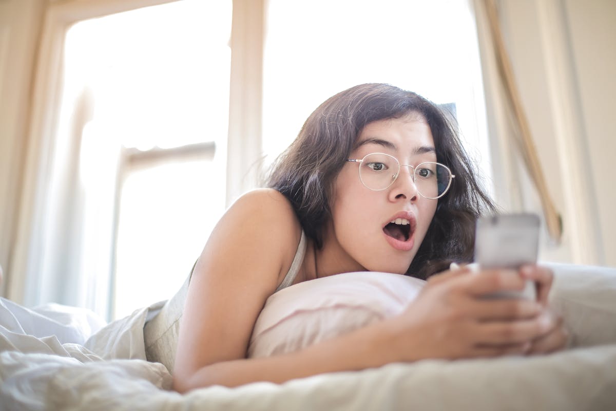 5 Apps que Revelam Curiosidades Sobre o Mundo ao Seu Redor Woman Lying on Bed Holding Smartphone