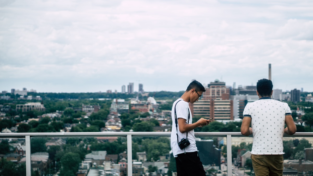 5 apps para traduzir conversas durante a viagem Two men are on a balcony overlooking the Toronto cityscape.
