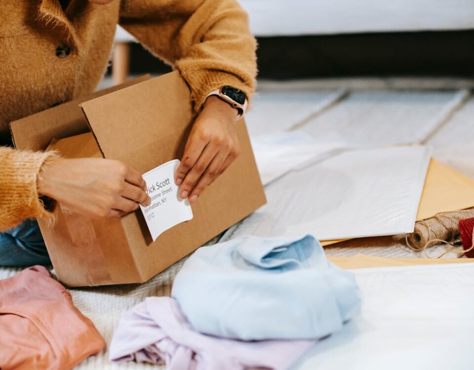 5 apps para comprar e revender roupas infantis A woman at home prepares a package for shipping, showcasing lifestyle and logistics.