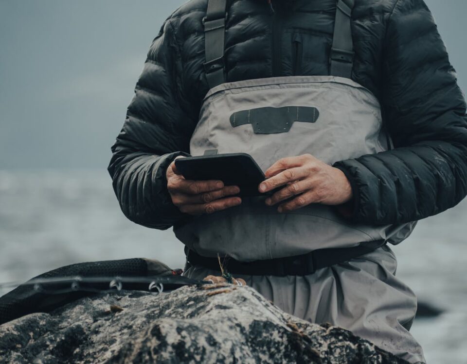 5 aplicativos para facilitar sua pescaria e encontrar o melhor ponto Man in protective clothing using tablet with gloves in cold, misty outdoor setting. Ideal for tech and outdoor adventure themes.