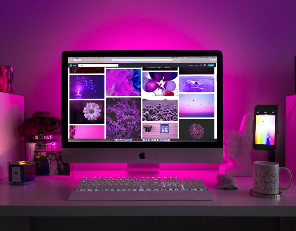 5 softwares para criar sites profissionais sem codificação Modern desk setup with neon lighting and a desktop computer displaying colorful images.