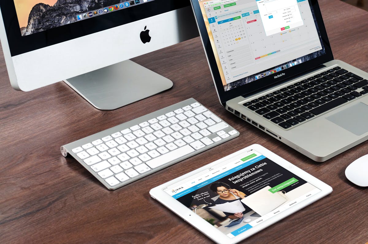 5 softwares para criar sites profissionais sem codificação A sleek office desk setup featuring Apple devices: iMac, MacBook, and iPad.