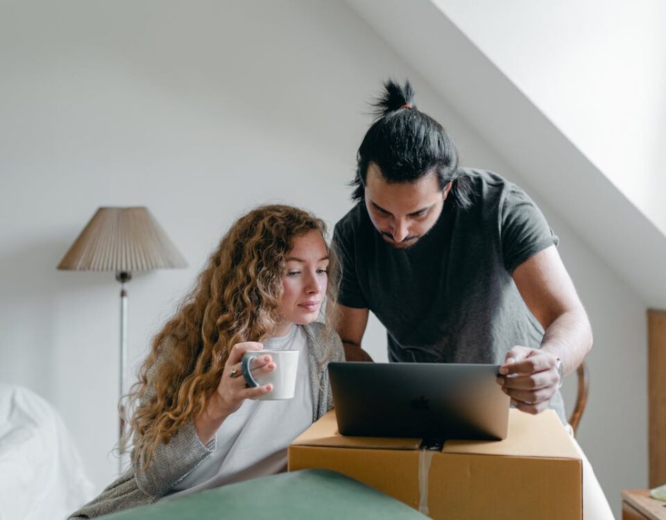 5 apps para encontrar imóveis sem complicação Concentrated young couple in casual outfit browsing netbook and packing stuff into carton boxes and suitcases to move out