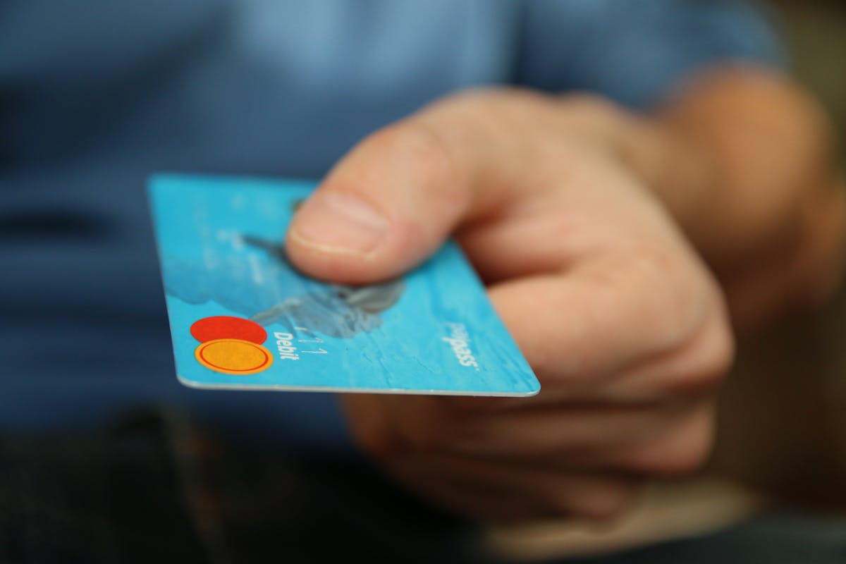 5 plataformas para acumular milhas e cashback em 2025 A close-up shot of a hand offering a blue debit card for payment.