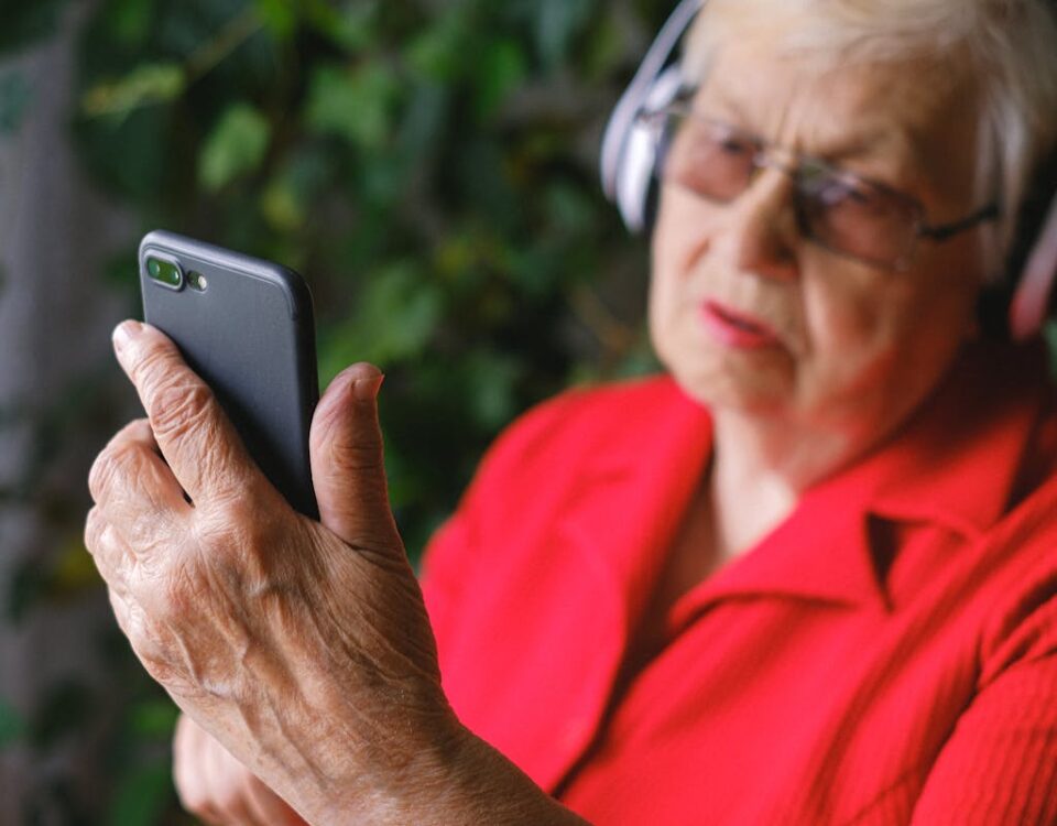 5 ferramentas para acompanhar política em tempo real Senior woman in red using smartphone with headphones outdoors.