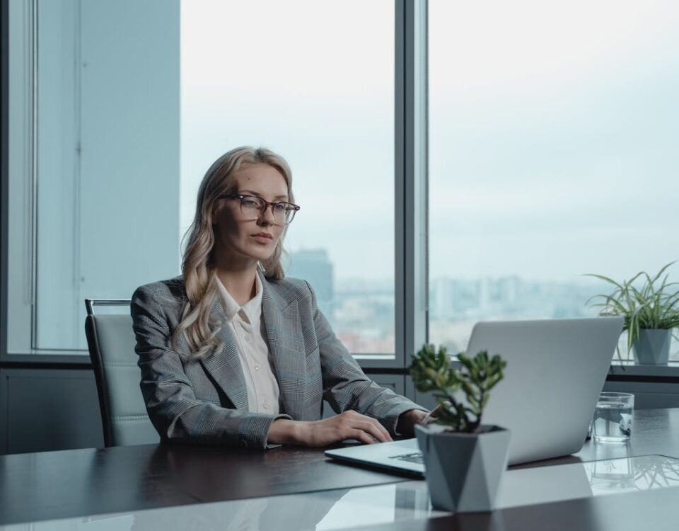 Benefícios do Software de Gestão de Férias da Bizneo A confident businesswoman in a grey suit working on a laptop in a modern office setting.