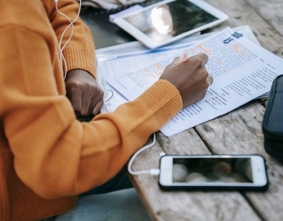 5 simuladores de trânsito para estudar a CNH From above of crop anonymous African American female in sweater studying and outlining words on paper at table with smartphone