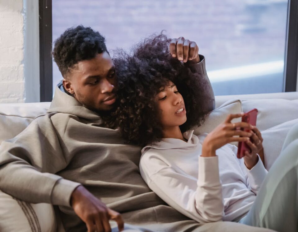 5 aplicativos para explorar o universo adulto com segurança Cozy image of a young couple relaxing on the couch at home, browsing a smartphone together.