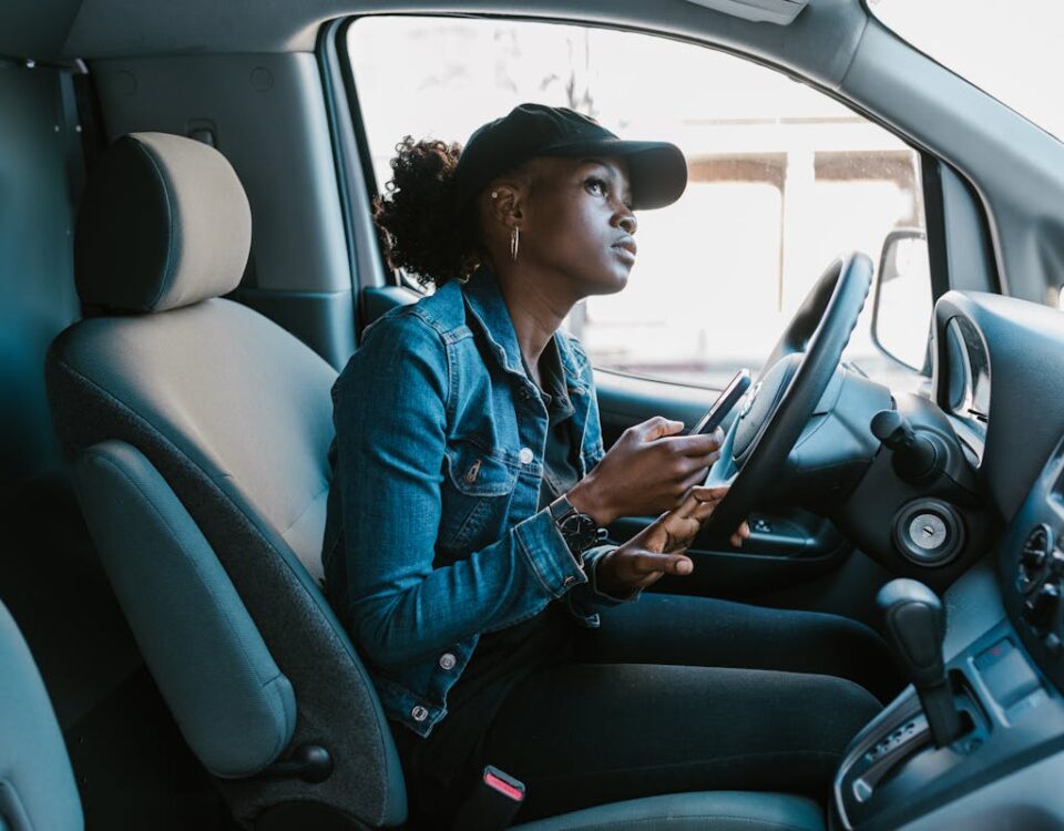 5 apps para gerenciar a validade da sua CNH A woman in a denim jacket focuses on her smartphone while sitting in a car driver's seat.