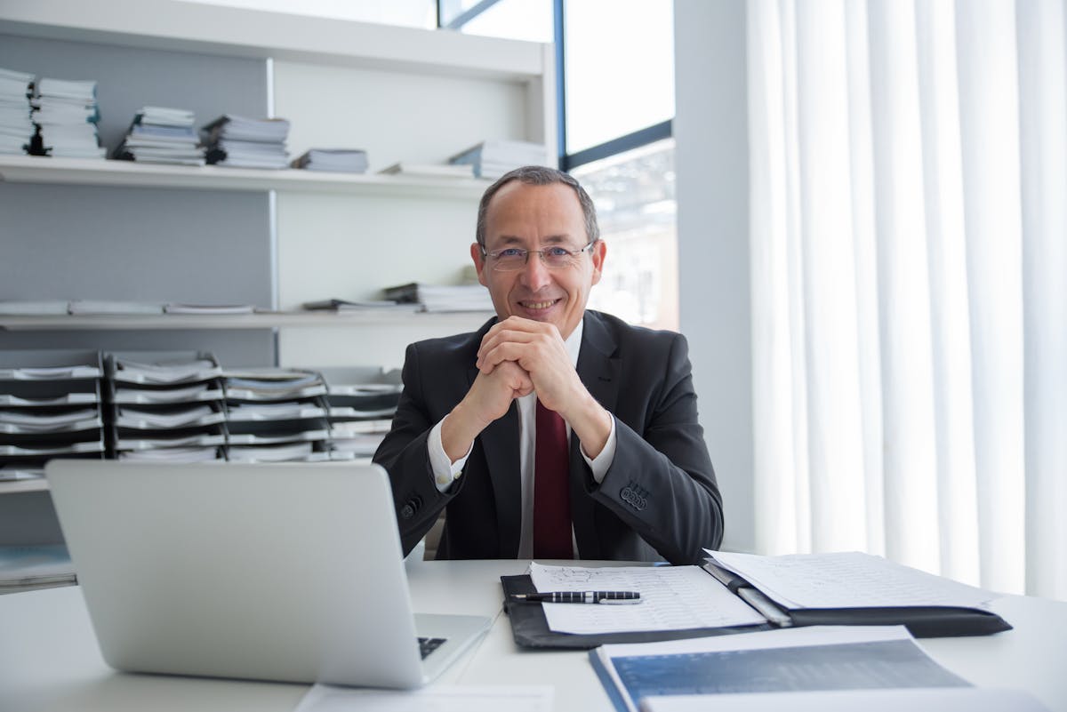 Smiling businessman in a suit with laptop and documents, exuding confidence.