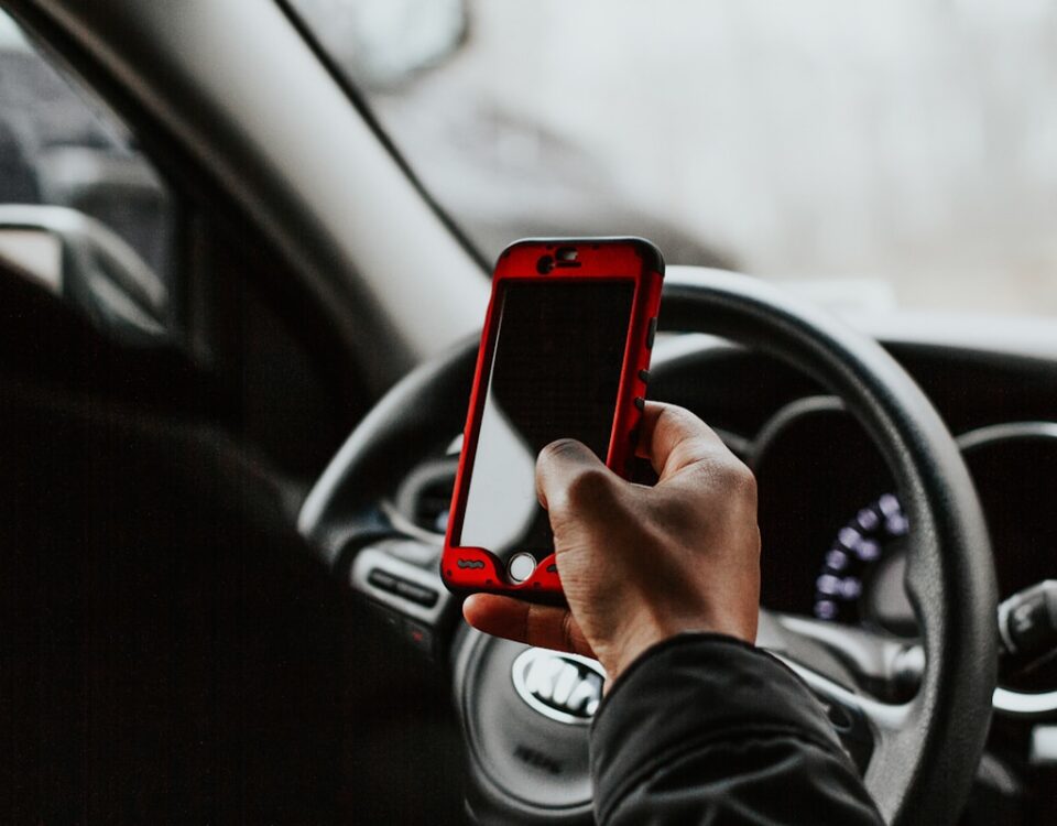5 apps para organizar sua documentação de CNH person holding red smartphone sitting in front of vehicle steering wheel