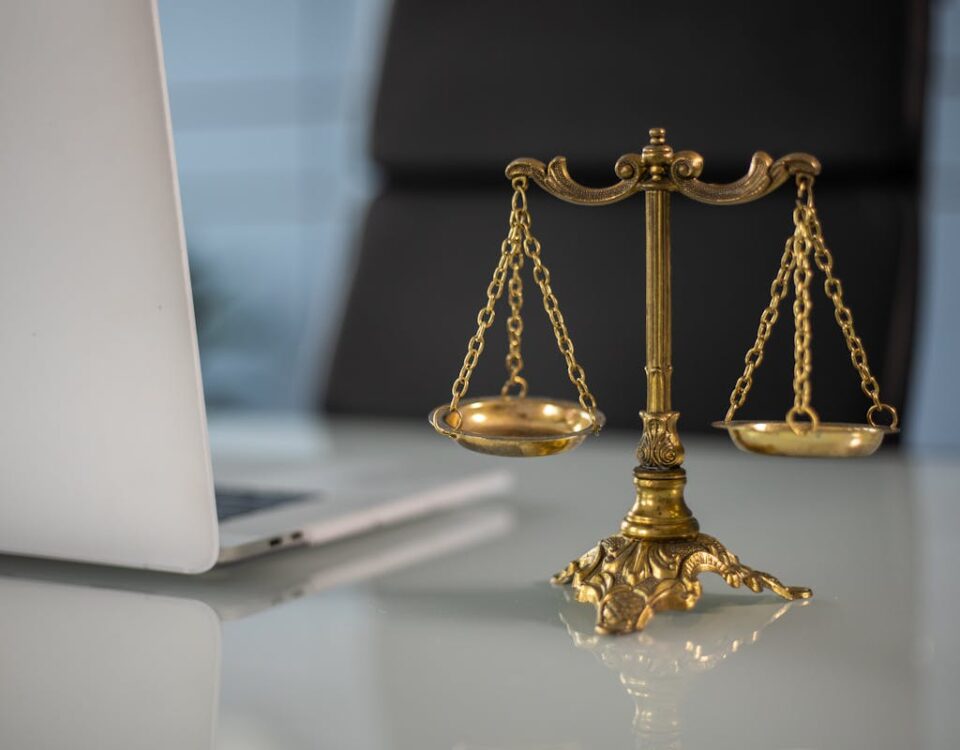 5 ferramentas para calcular honorários de advogados Golden justice scales on a desk beside a laptop, symbolizing law and balance.