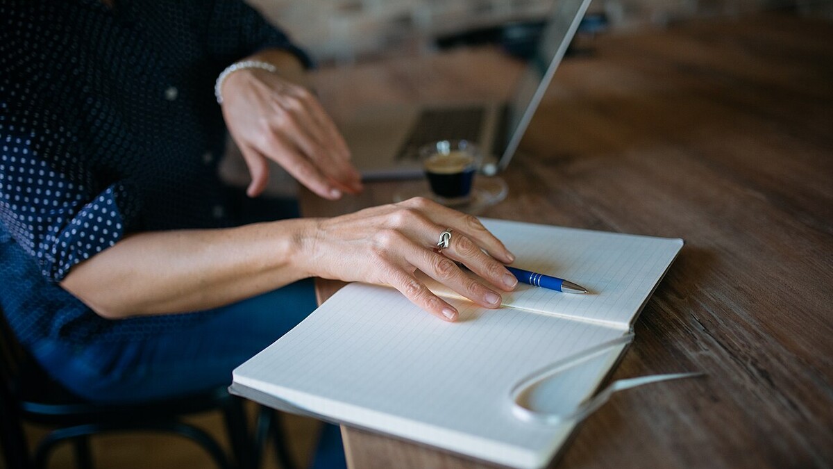 Apps ajudam a repetir a receita perfeita de café em casa? Mãos anotando em caderno ao lado de notebook e xícara de café