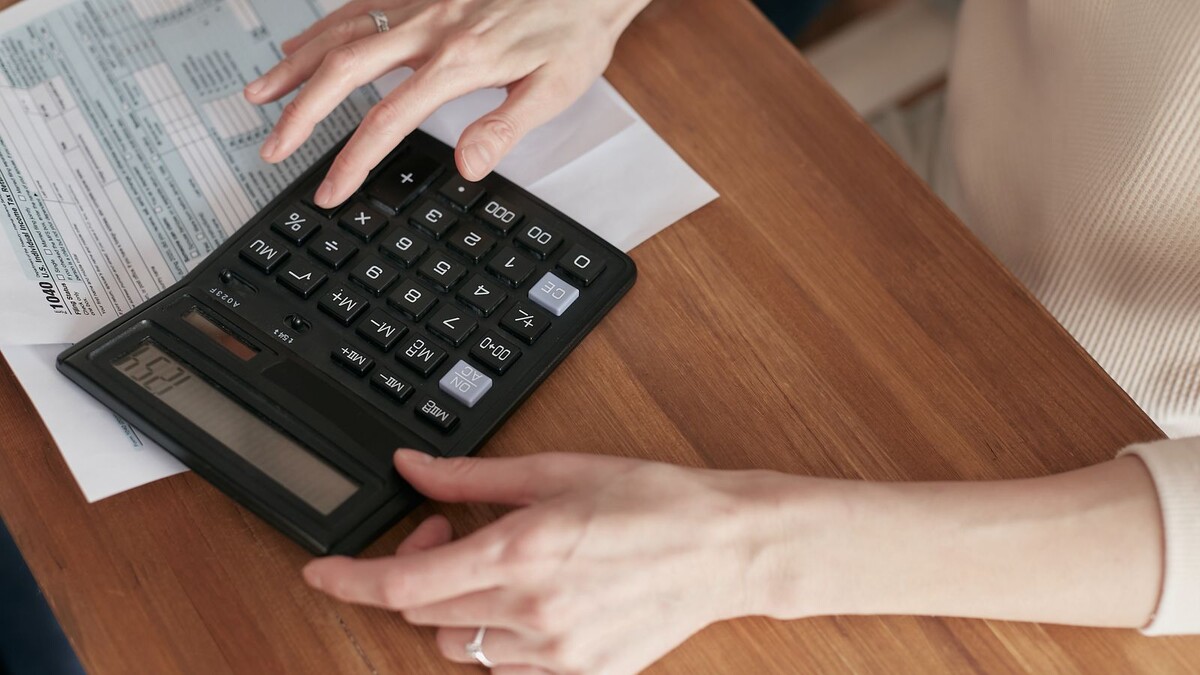 Mãos de uma mulher usando calculadora sobre contas em uma mesa de madeira