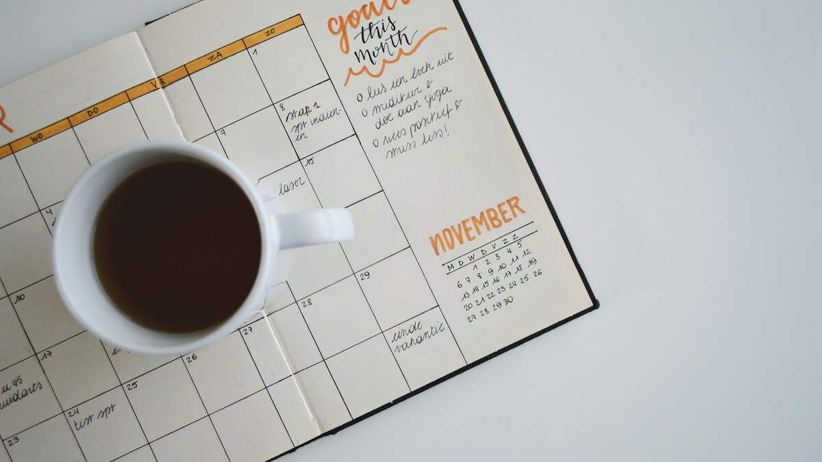 Como escolher um app de escala e banco de horas para a equipe? Calendário de papel com xícara de café ao lado, usado para planejar a semana