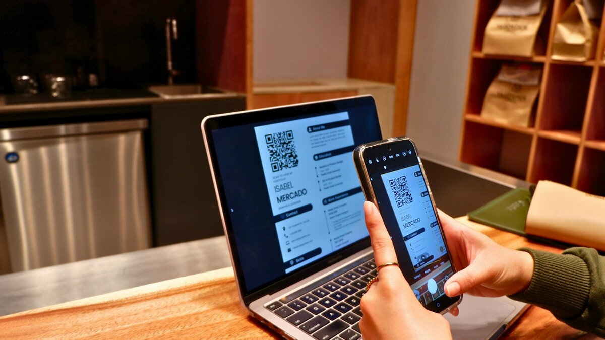 Gerador de link para WhatsApp grátis: o que conferir antes de usar Pessoa segurando um celular com QR Code na tela diante de um notebook aberto sobre mesa de madeira