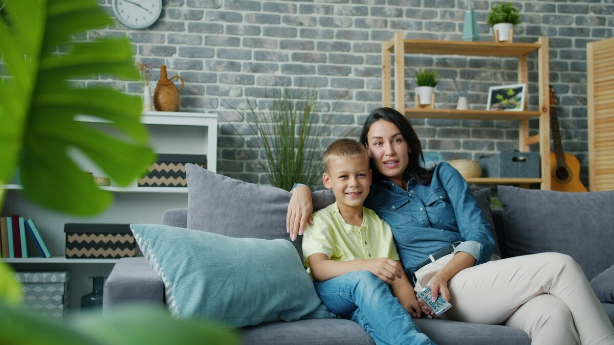 Mãe e filho sentados no sofá da sala olhando para a televisão