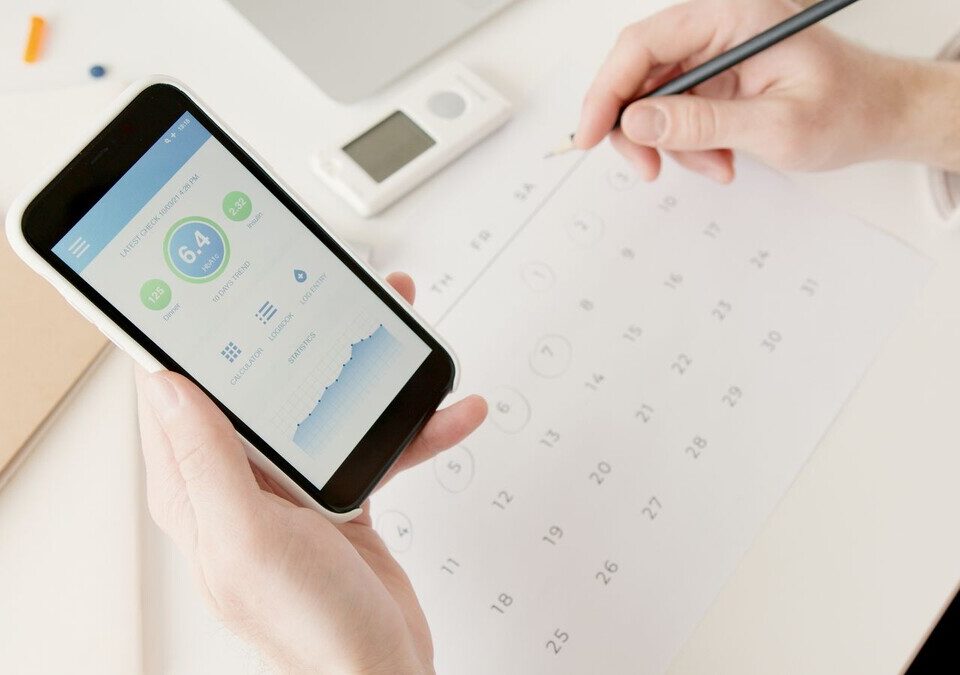 Onde guardar laudos de exames no celular sem perder o histórico Mãos segurando um celular com gráficos de saúde ao lado de um calendário