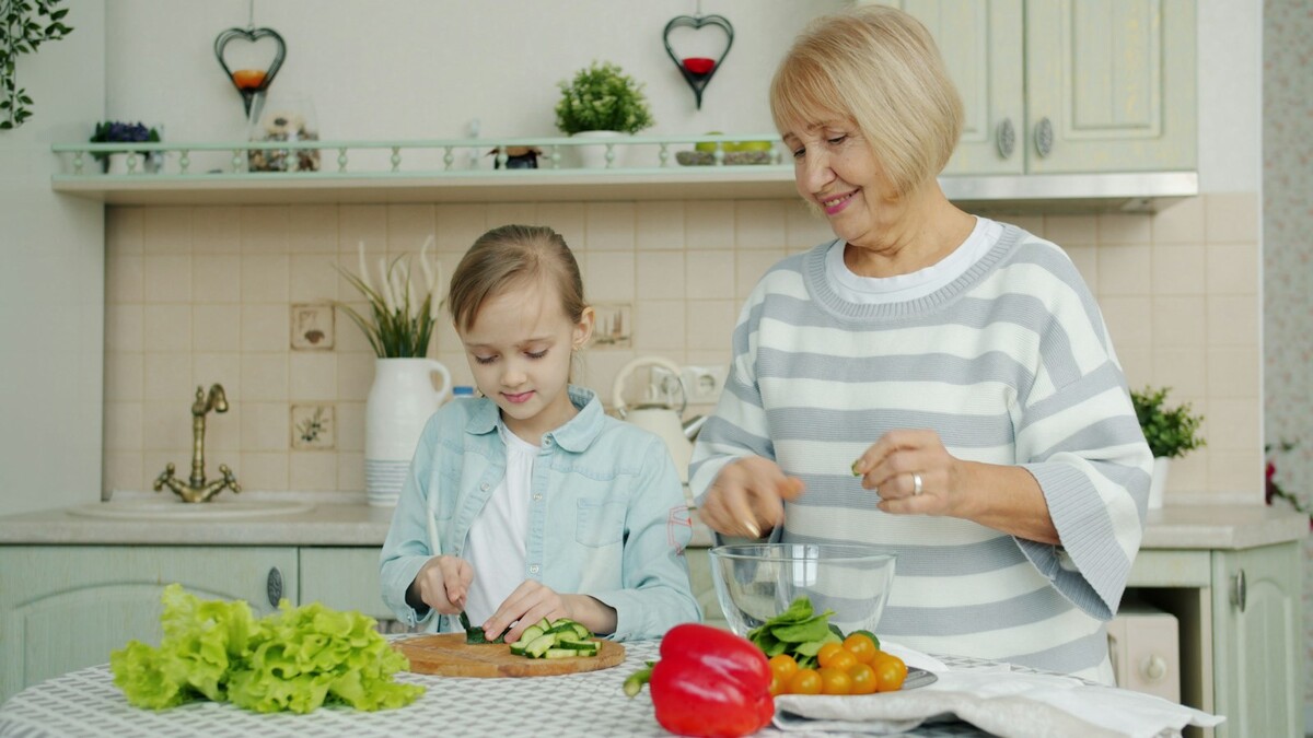 Quais apps ajudam a aproveitar o único dia de folga da semana? Mulher mais velha e uma menina cortando legumes juntas em uma cozinha