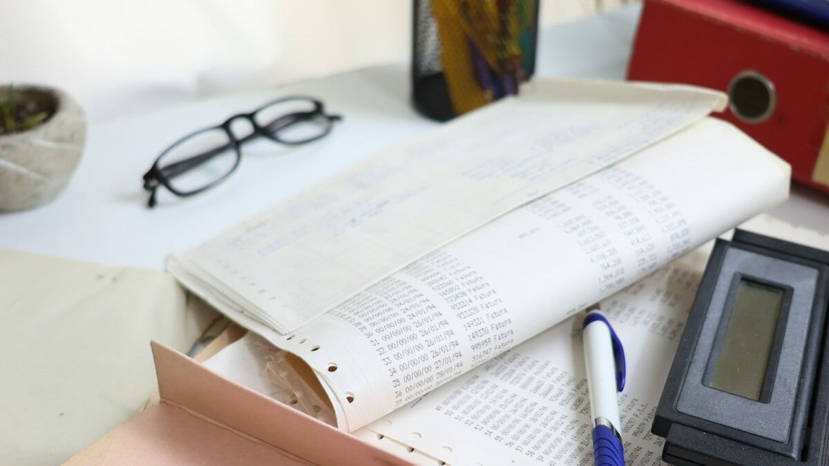 Mesa com papéis, óculos, calculadora e material de escritório