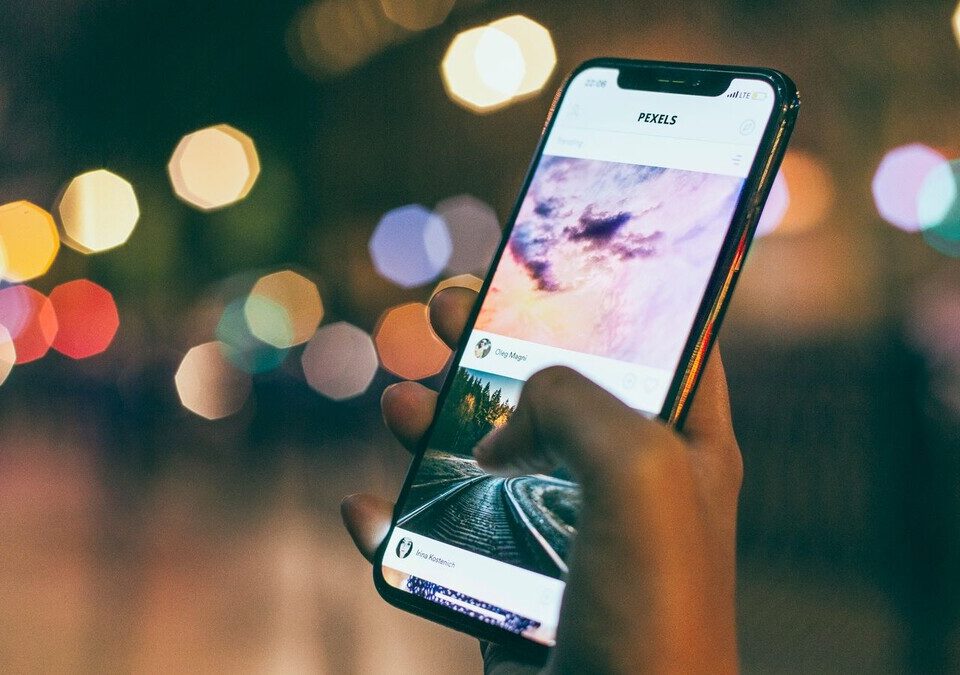 Mão segurando um celular com aplicativo aberto à noite, com luzes desfocadas ao fundo
